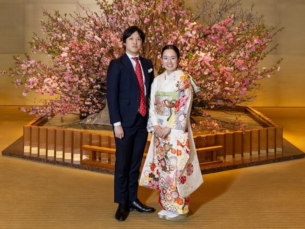 Formal engagement photo of Arisa in traditional white kimono and Yuichiro in navy suit, posed elegantly with cherry blossoms and modern lighting